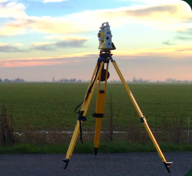 A survey total station on a tripod in a field at sunset